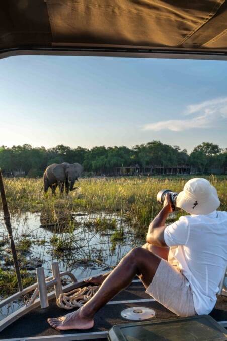 Man on edge of boat photographing elephant in water